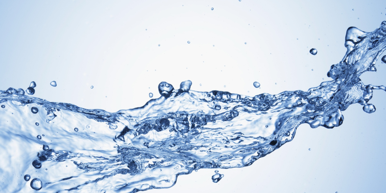 Close-up of clear water splashing against a light blue background with visible droplets and motion.