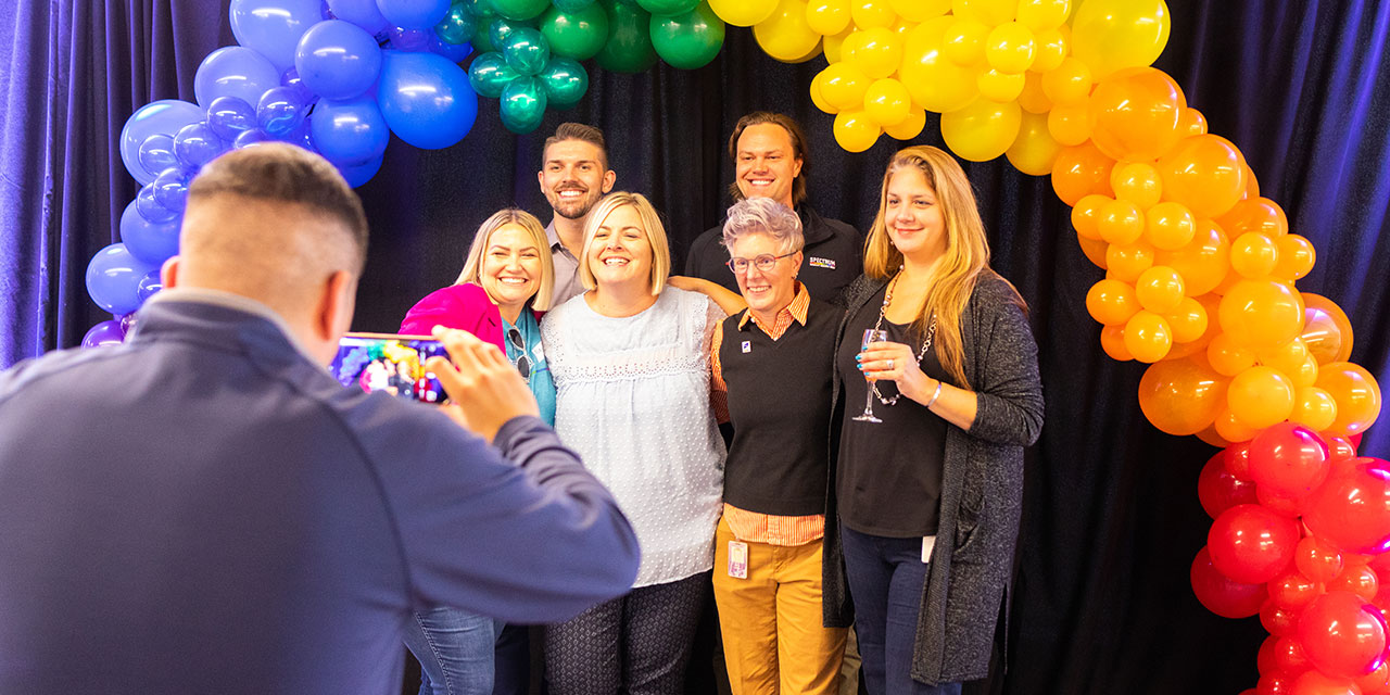 A group of Silver Lakeassociates pose for a photo under an arch of rainbow colored balloons at a corporate event