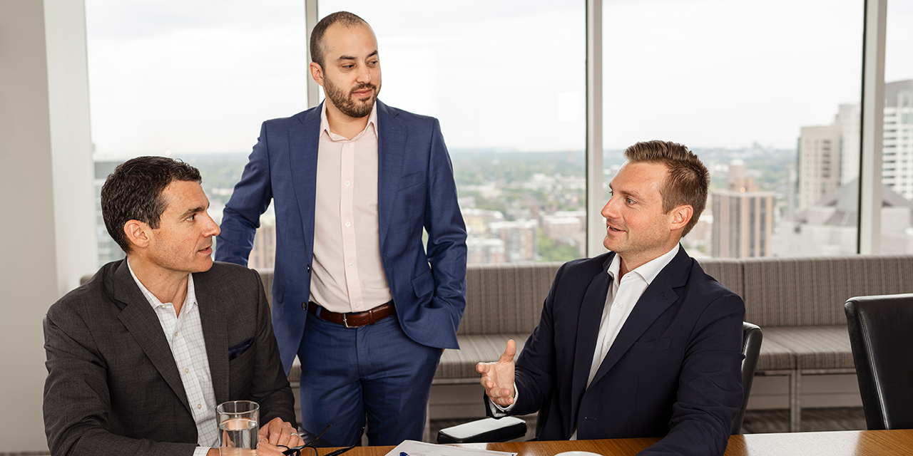 Three men wearing suits taking in a meeting room.